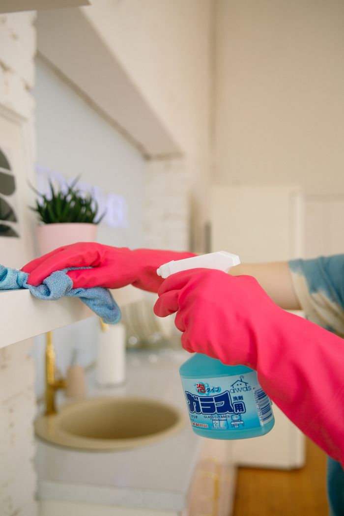 gallery-3 Person using spray bottle and cloth for cleaning a kitchen shelf, ensuring hygiene and cleanliness.